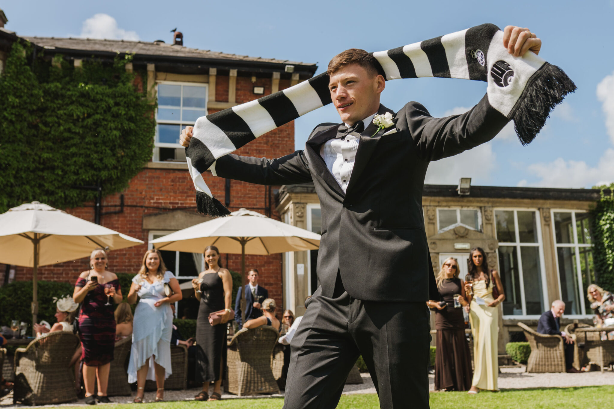Groom holding his Newcastle United football scarf up in front of laughing guests