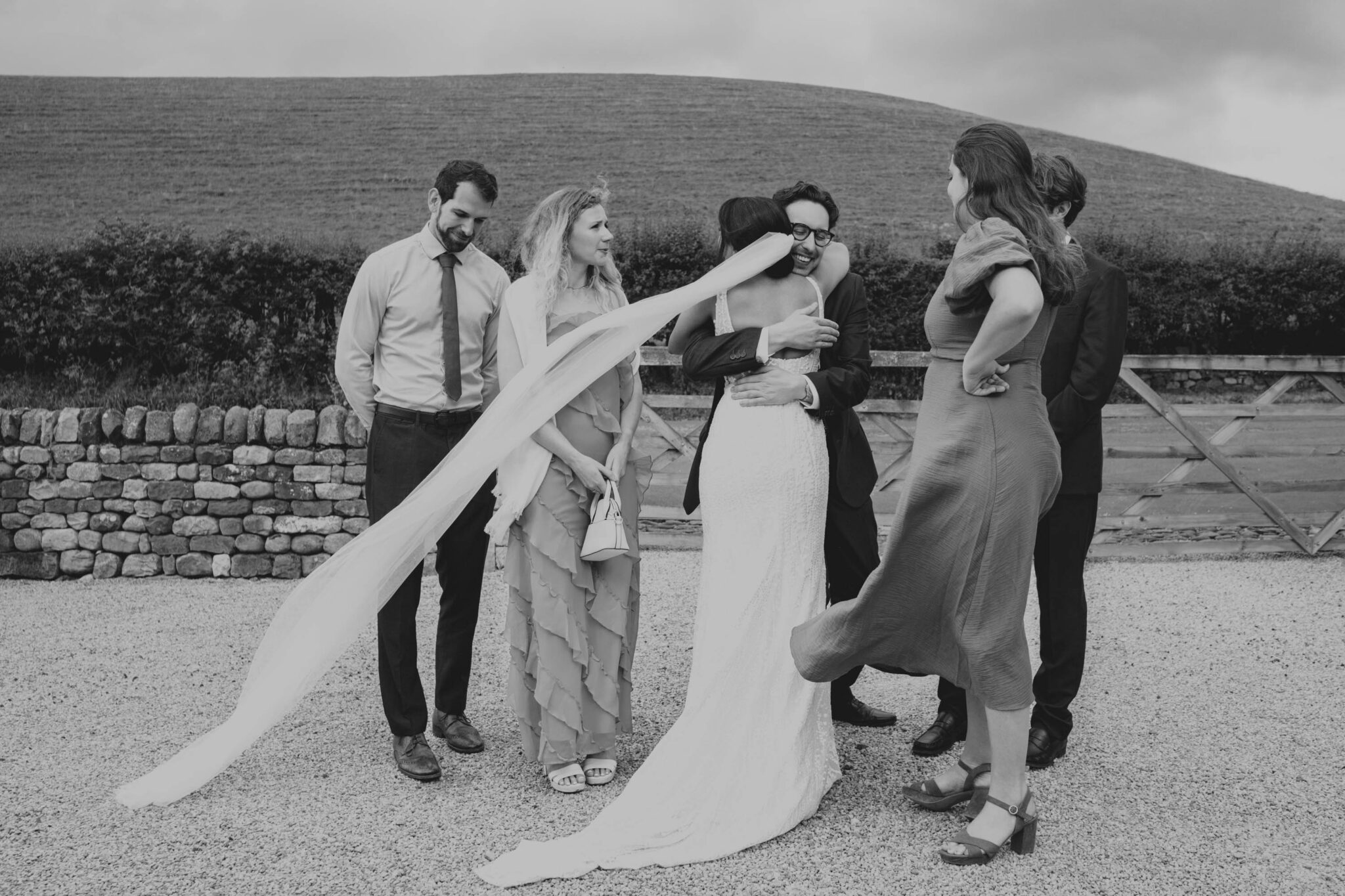 Bride hugging guests with vale flowing in the wind.